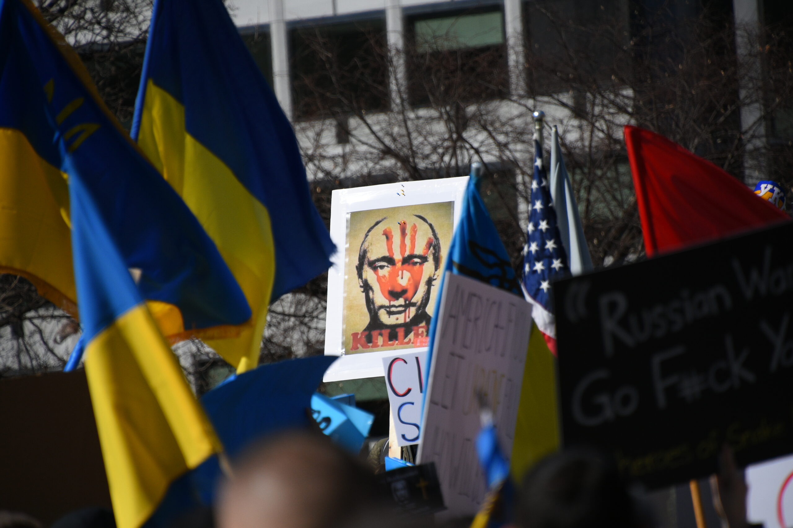 Kuva mielenosoituksesta. Kuvassa näkyy Ukrainan sini-keltaisia lippuja sekä kyltti, jossa on Vladimir Putinin tahrittu kuva.